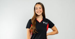 A young woman with long brown hair wearing a black and red Ball State collared shirt, posing and smiling in front of a white backdrop.