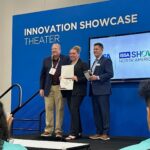 Ball State student receives a Global Consultative Sales Excellence certificate from two men on stage at the ISSA Show Innovation Showcase.