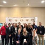 Group of 14 Ball State students and faculty smiling in front of an International Collegiate Sales Competition (ICSC) banner.