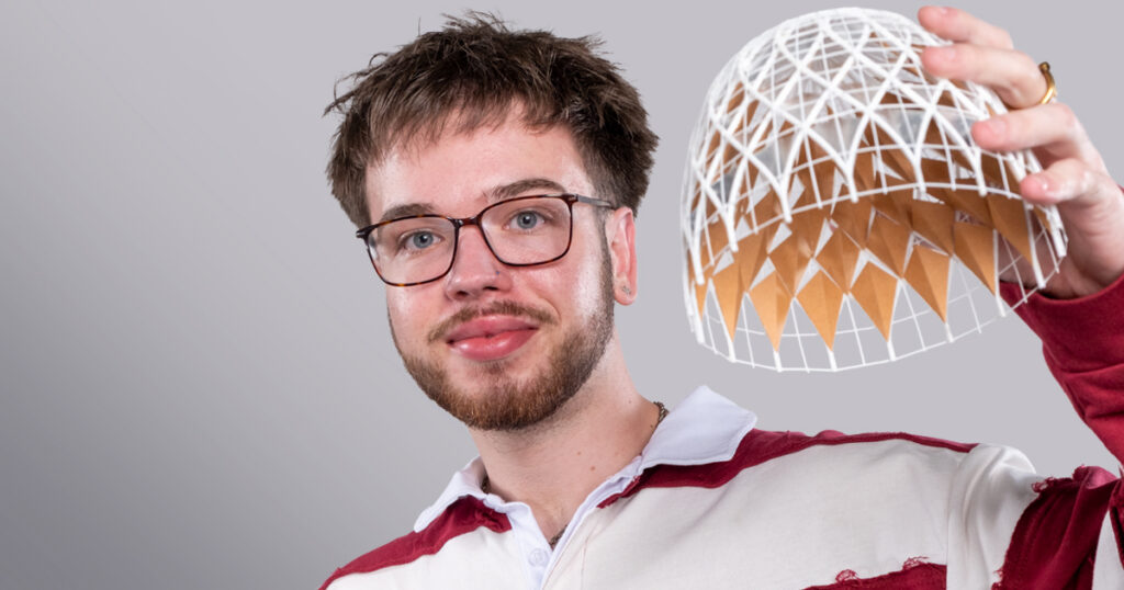 Brodie Budzinski, a young man with short brown hair, brown facial hair, wearing glasses and a red and white striped sweatshirt and holding up a weaved 3D model