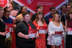 A group of students holding red and white award certificates, standing in front of a Ball State University banner.