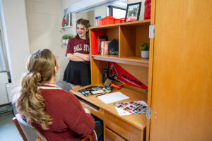 Roommates talking at a desk in a dorm room.