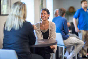 Two people sit in a meeting, and one smiles brightly.