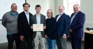 Group of six men pose together as one holds a certificate recognizing an innovation challenge award.