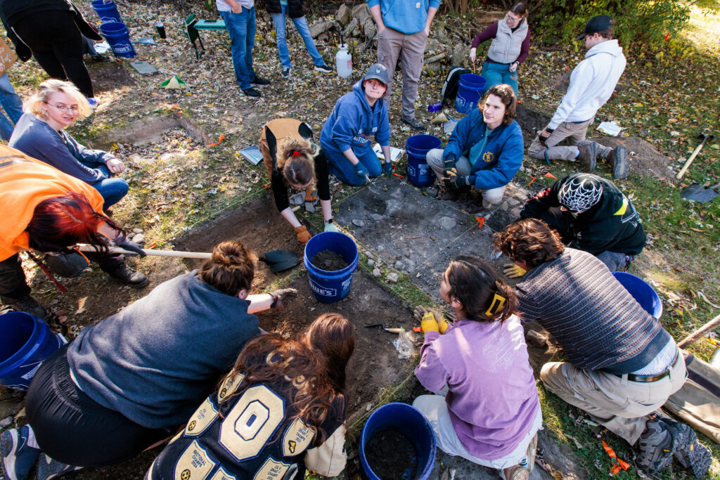 Students on the ground outside with shoves and spades digging in sectioned squares.