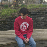 Young man in a red shirt sitting on stone ledge.