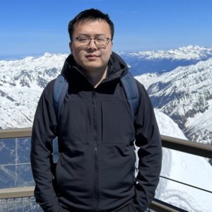 an asian man with glasses is wearing a winter coat outside with a snowy mountain view behind him