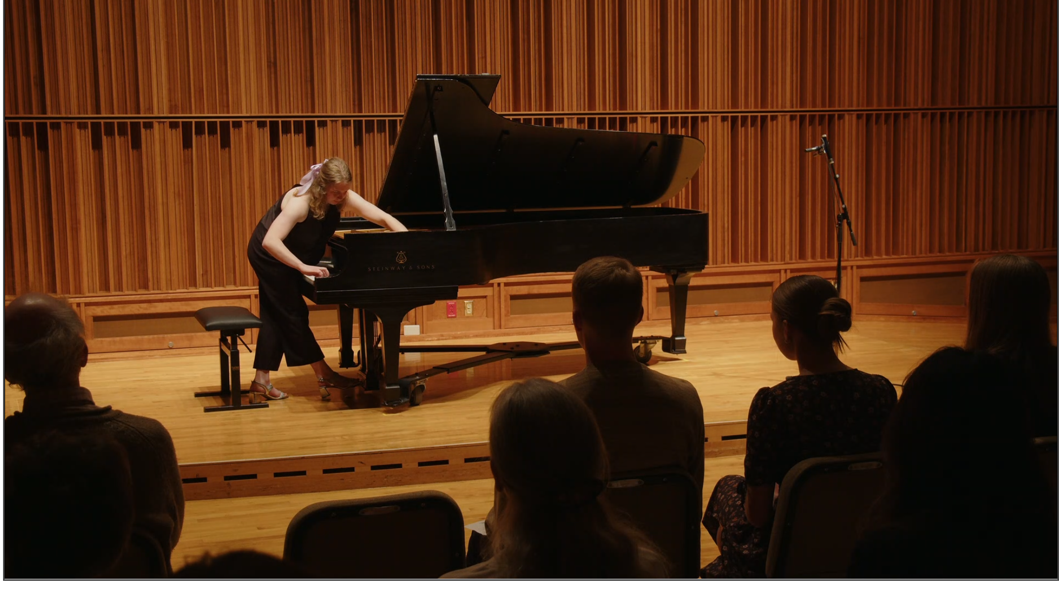 Alena performs using a piano in front of an audience.