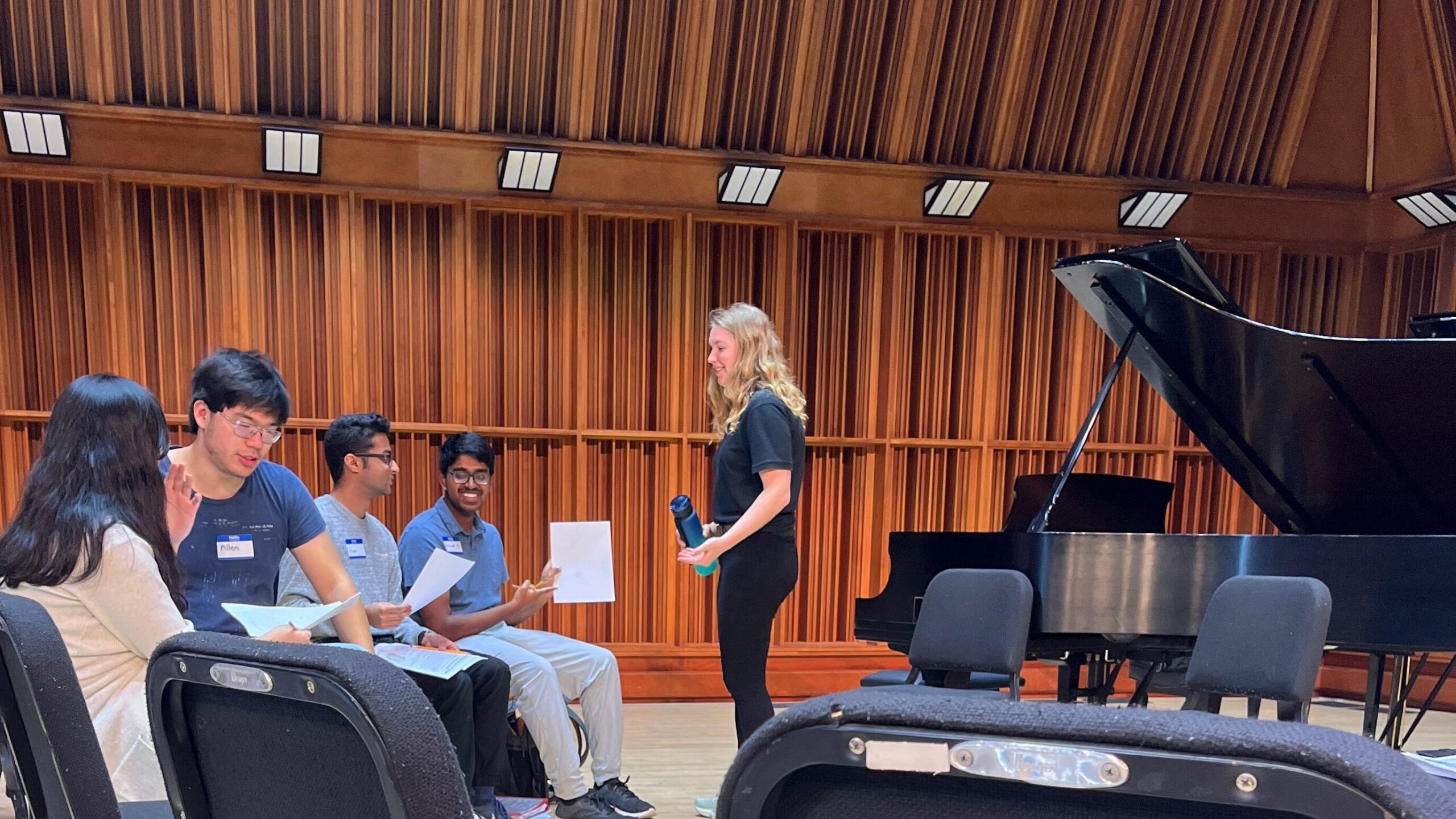 Alena stands next to a piano and coaches music student
