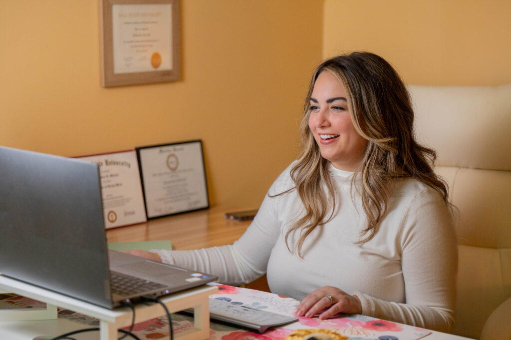Woman sitting at a desk working on her computer with Ball State University Bachelor of Social Work Degree in the background