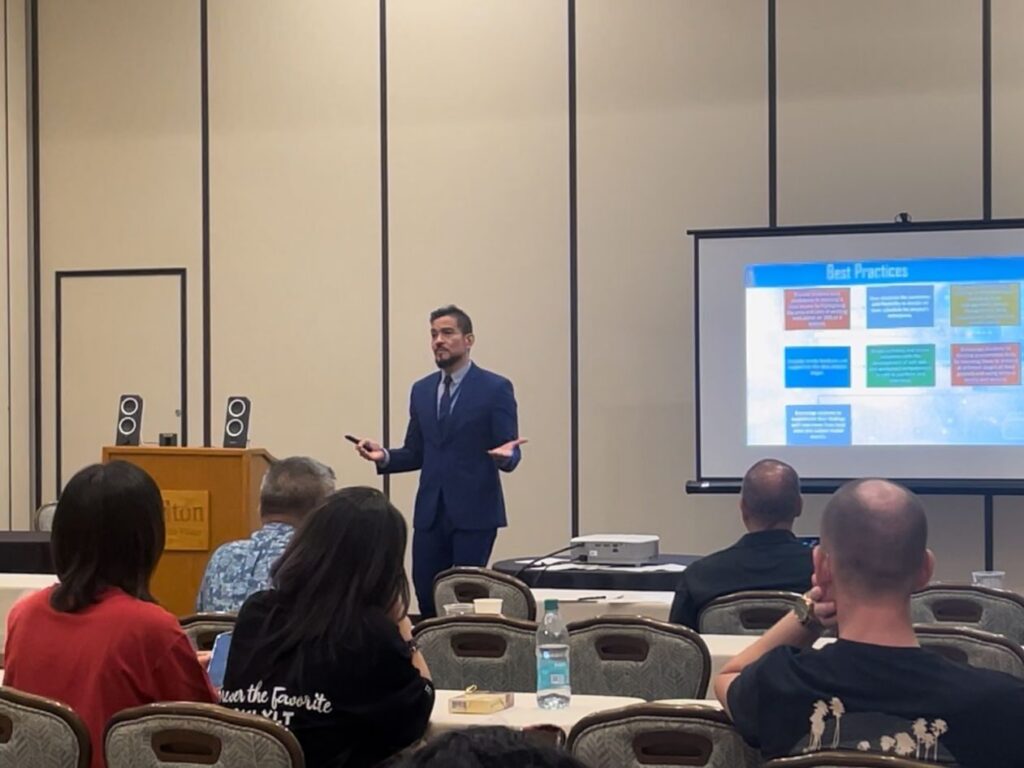Dr. Luis Orozco presents at the Hawaii International Conference on System Sciences in front of a room of people.