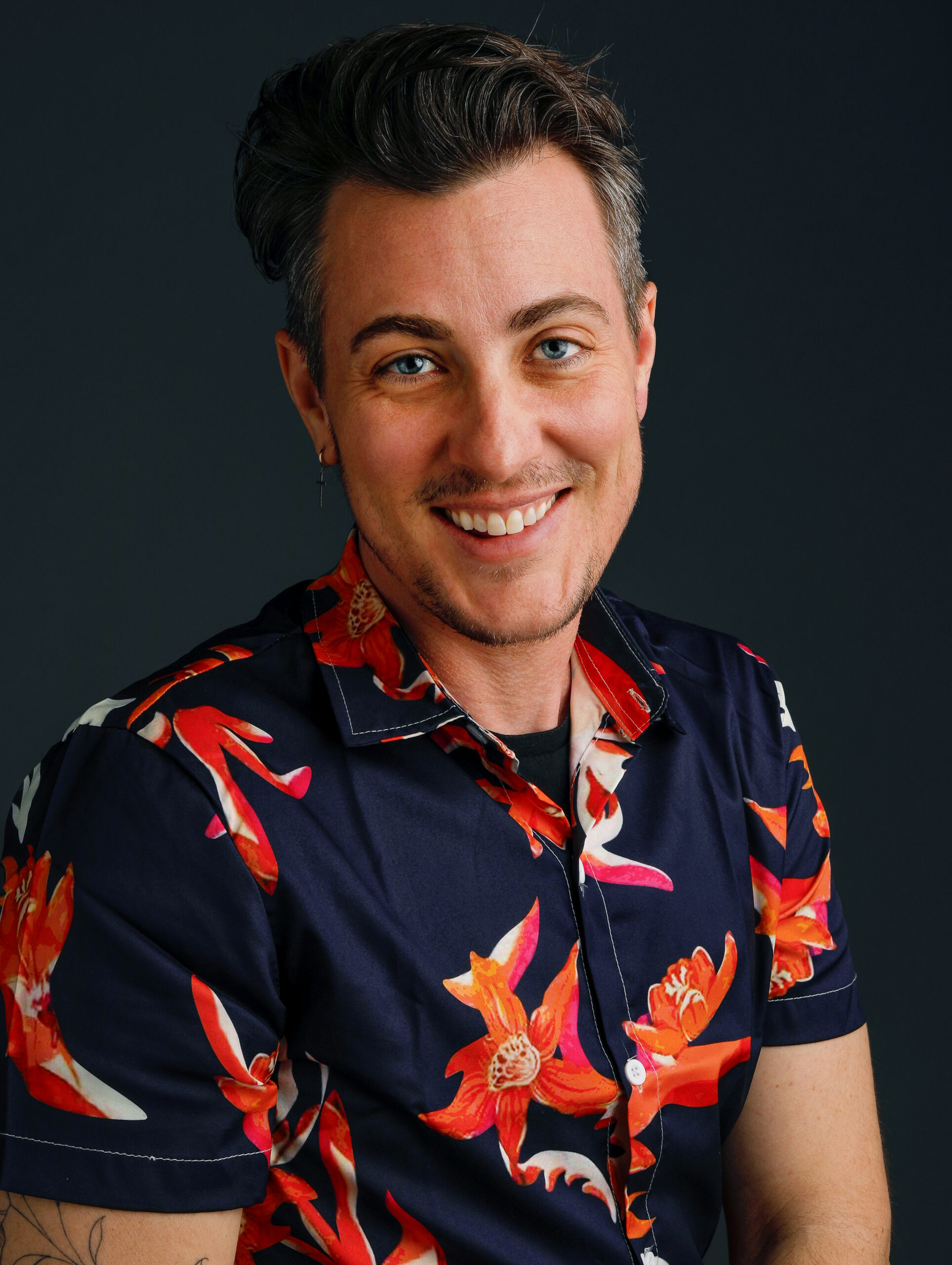 Leo Caldwell poses for a professional headshot wearing a colorful floral print shirt against a dark background.