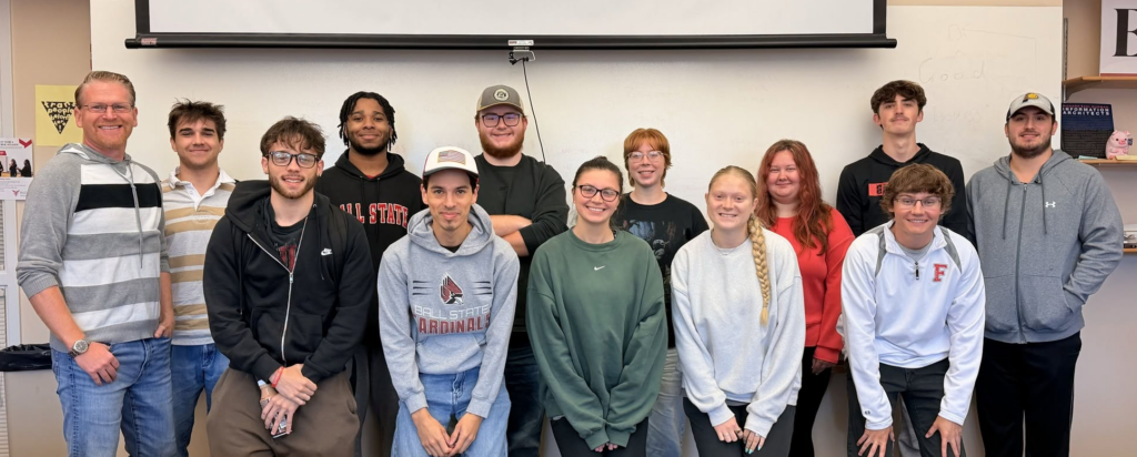 Dr. Adam Kuban stands with his Journalism 322 class for a photo in a classroom.