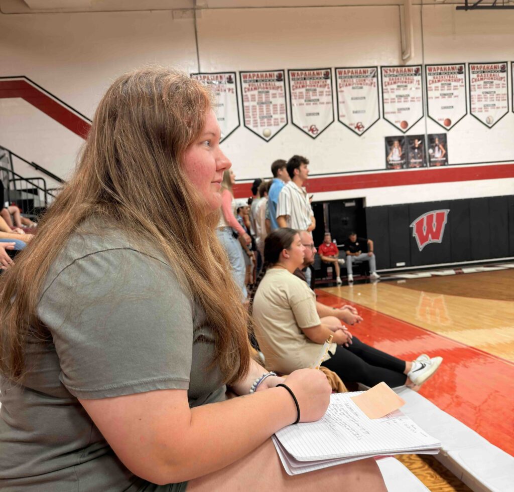 Journalism 322 student Emma Bergman sits at a high school volleyball game taking notes.