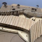 Scale model of the Flexus project made of wood dowels and tag board. The roof has four rectangular pieces curved around the center of the building.