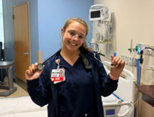 Taylor Burket dressed in her scrubs as a Nurse holding a stethoscope.