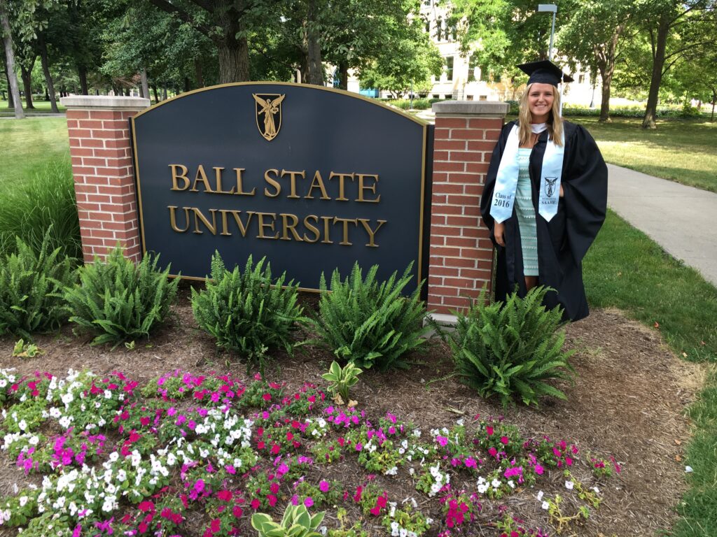 Jordyn standing by the Ball State University sign, dressed in a cap and gown.