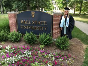 Jordyn standing by the Ball State University sign, dressed in a cap and gown.