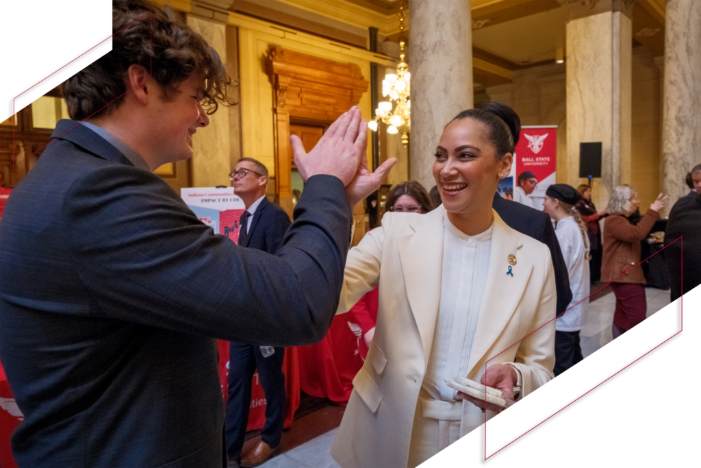 A Ball State student and a woman in professional attire smile and high-five during a gathering inside the Indiana Statehouse.
