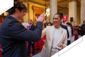 A Ball State student and a woman in professional attire smile and high-five during a gathering inside the Indiana Statehouse.