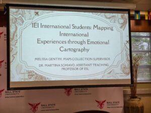 Powerpoint presentation on projector screen that says "IEI International Student: Mapping International Experiences through Emotional Cartography" by Melissa Gentry and Dr. Martina Schiavo