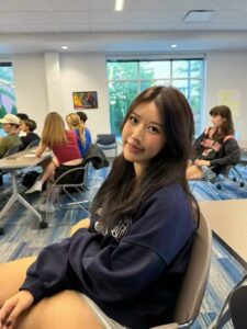 Jasmine Zhuang is sitting on a chair in a classroom.