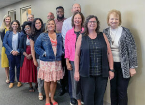 Marilynn Quick stands at the far right as 12 members of the Department of Educational Leadership, including faculty and staff, pose together for a group photo in a hallway.