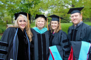 Marilynn Quick poses outdoors with three graduates, all wearing academic regalia, during Ball State’s Spring 2014 Commencement.