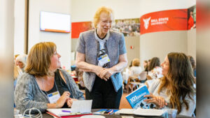 Marilynn Quick stands between two younger women at a table as they smile and talk during the Indiana School Counselor and Administrator Collaboration Institute at the Ball State Alumni Center in June 2022.