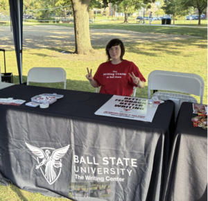 Writing Center tutor sitting at a table ready to greet Star Party visitors.