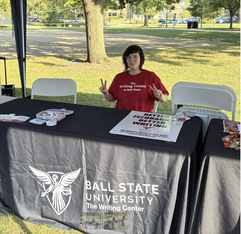 Writing Center tutor sitting at a table ready to greet Star Party visitors.