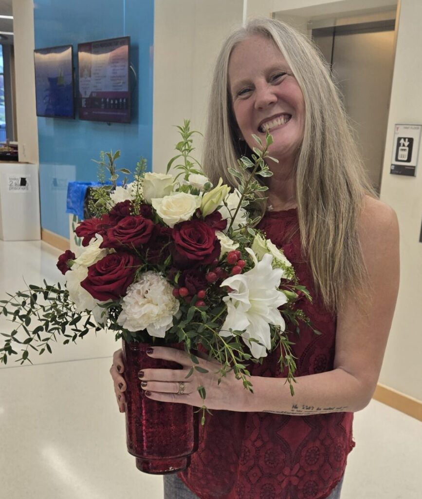 Dr. Greta Slater, smiling, holding a glass vase of red and white roses with greenery. 
