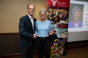 Ball State University President Geoff Mearns Shakes hands with Dr. Mary Provence as she accepts her Immersive Learning Award. Mary is holding the award in her right hand. It is clear glass with tiny writing on it, which is not legible in the photo.