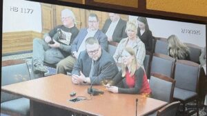 You can see the outline of a TV screen, where the video of the Indiana Statehouse Broadcast was being played. The main focus of the image is Sam Snideman on the left sitting at a desk, and beside him is MSW Intern Erica Smatlak. There is a long microphone in front of them, and they appear to be speaking. You can see 3 males and three females sitting behind them in gallery seating. They have varied facial expressions. The words HB 1177 and the date 2/10/2025 appear in the upper corners of the image.