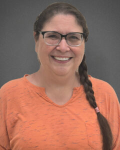 Headshot of Brandy LoPilato She is Caucasian and wearing an orange shirt, and has long straight brown hair styled into a braid. She is smiling.