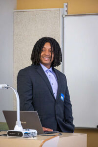 James Ramsey presenting at Portfolio Day in professional attire, smiling. 