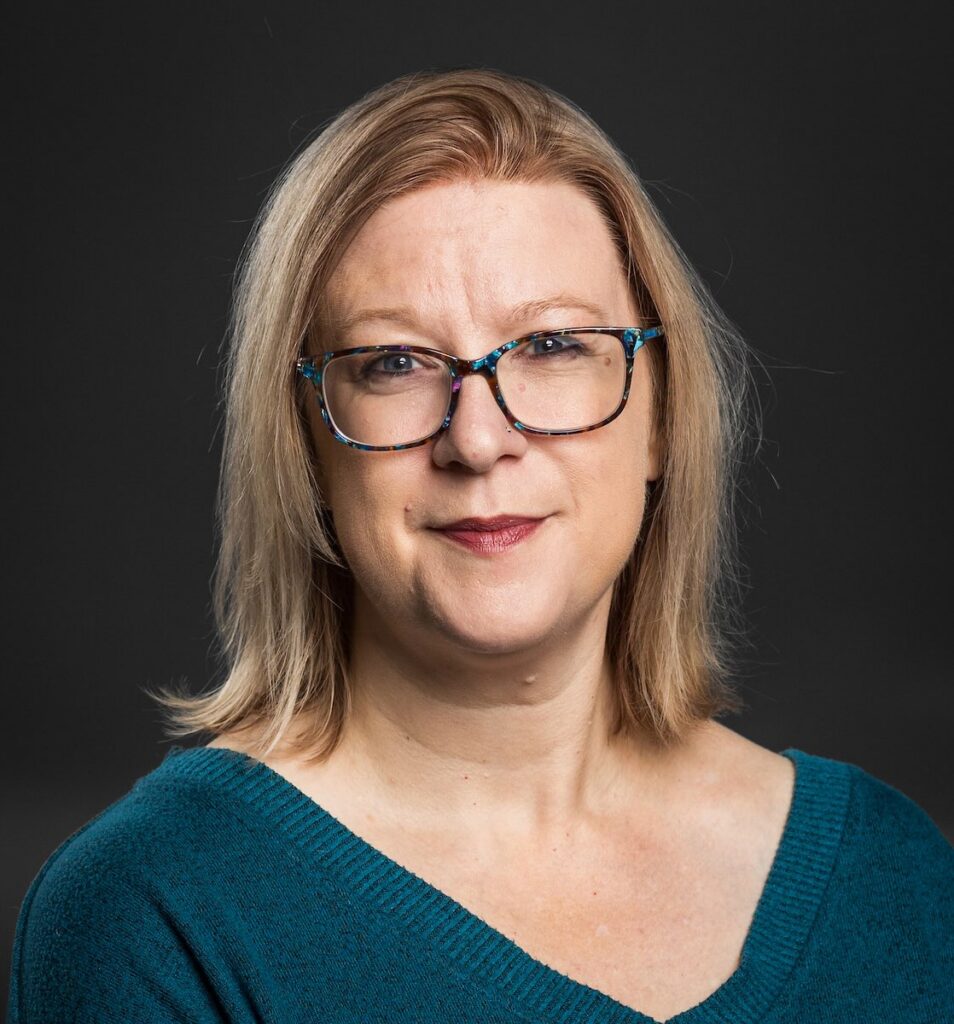 a woman with blonde hair and glasses and a teal shirt