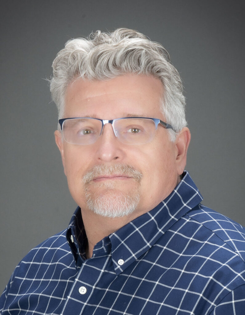 a man with blue checked shirt, grey hair, and glasses