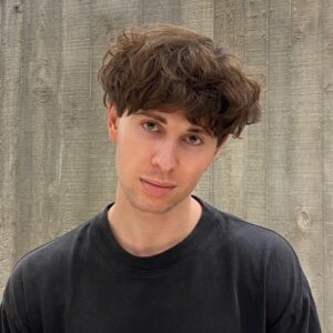 young man with brown hair in front of wood paneling