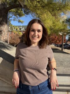 young woman with auburn hair in front of trees and building